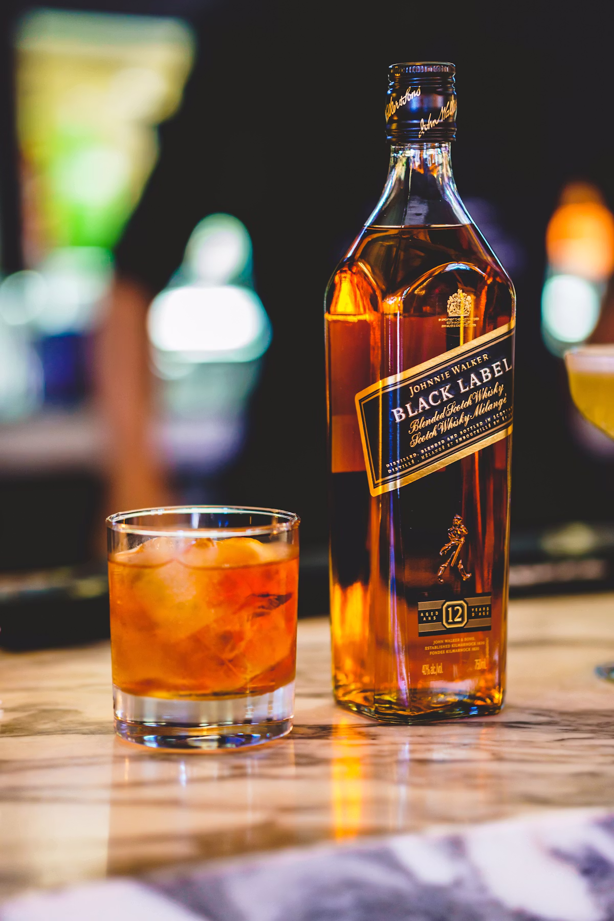 Glass of amber spirit poured beside vintage cellar bottles